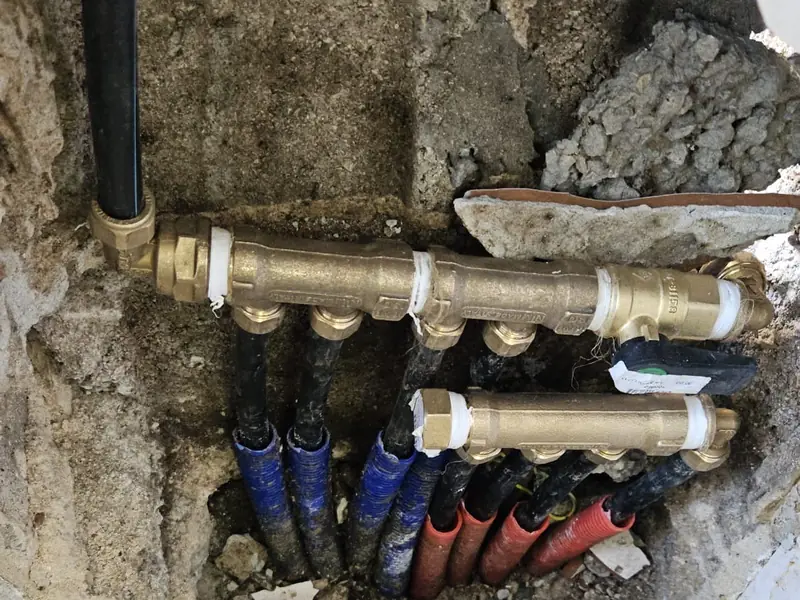 מחלק מים מפליז עם צינורות כחולים ואדומים, בתוך קיר פתוח
